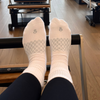 Person wearing hipSwan white crew grip socks with a compression arch pattern on a Pilates reformer machine.