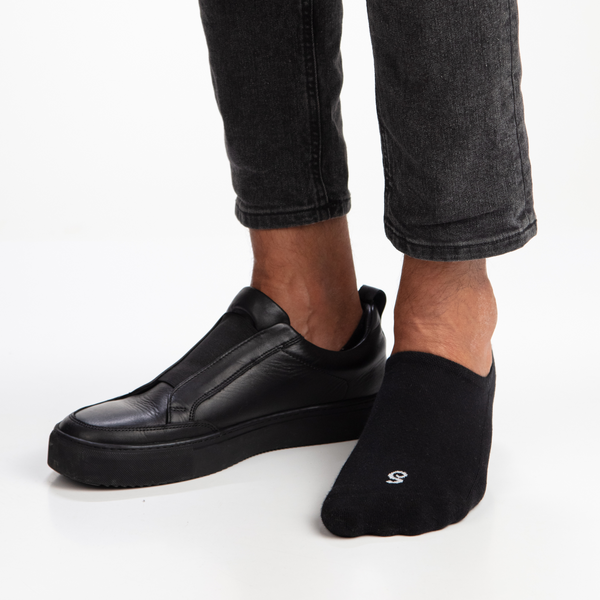 Man wearing black slip-on shoes and black organic combed cotton no show no see invisible socks on a white background