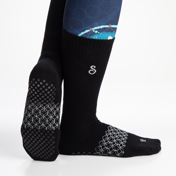 Black crew length grip socks with silicone sole grips, compression arch band, and fully cushioned footbed on a white background